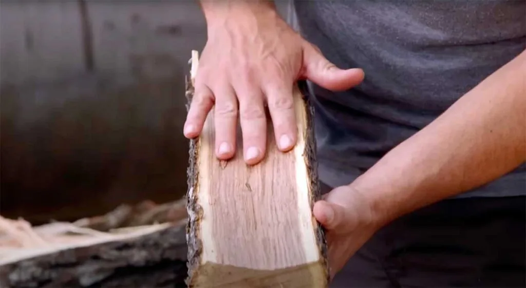 Hands holding a split log of mesquite firewood, showing red interior wood.