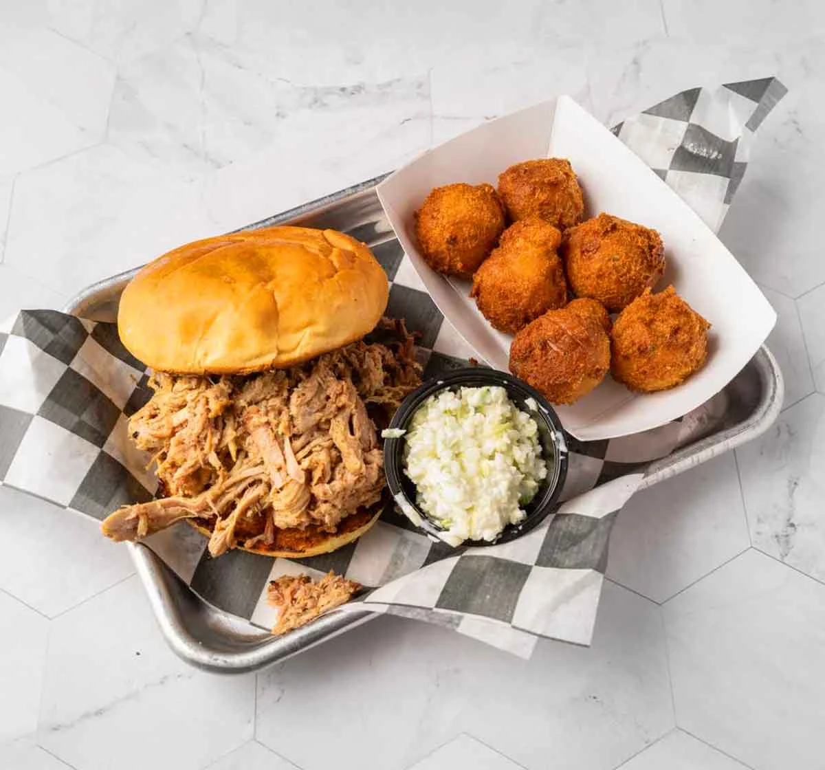 Pulled pork sandwich, slaw, and hush puppies on metal serving tray.
