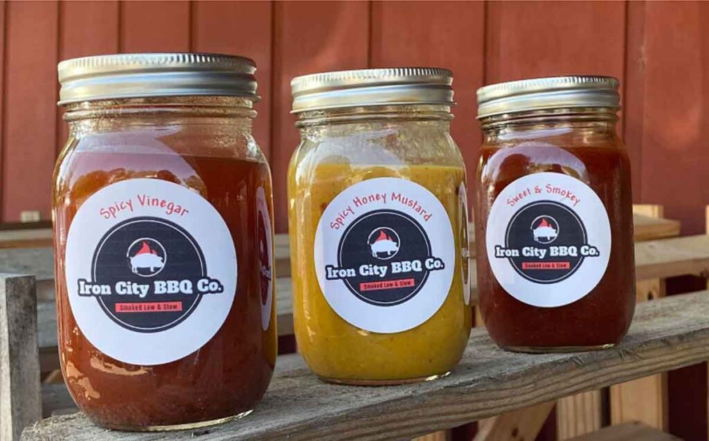 Three mason jars, each with a different sauce from Iron City BBQ.