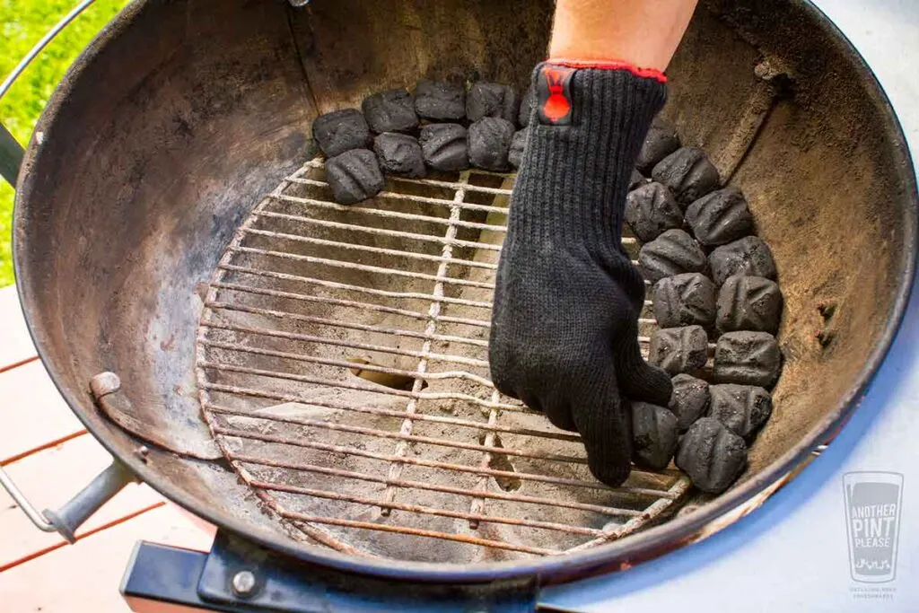 Hand inside Weber kettle grill placing charcoal briquettes in a row following the snake method.