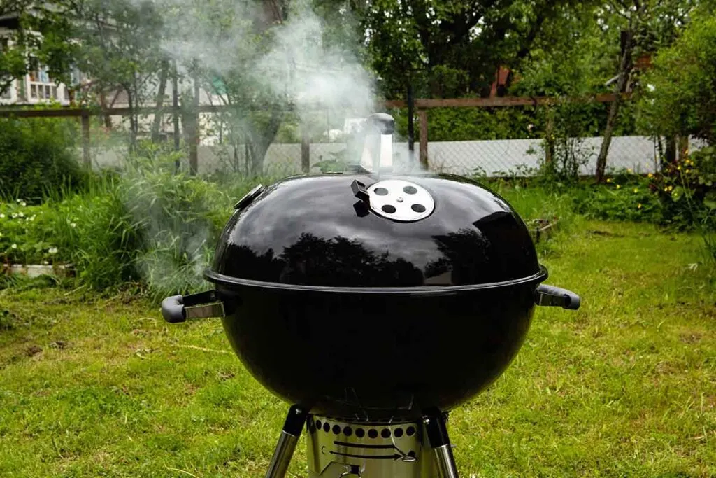 Weber kettle grill with smoke coming from vents.