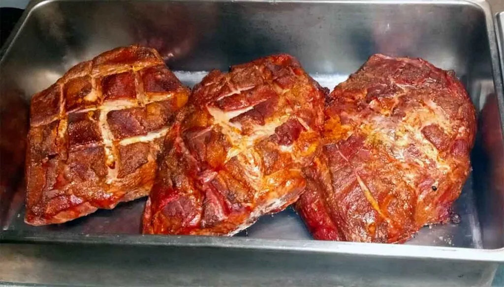 Smoked pork shoulders with crosshatched bark, ready for pulled-pork service.