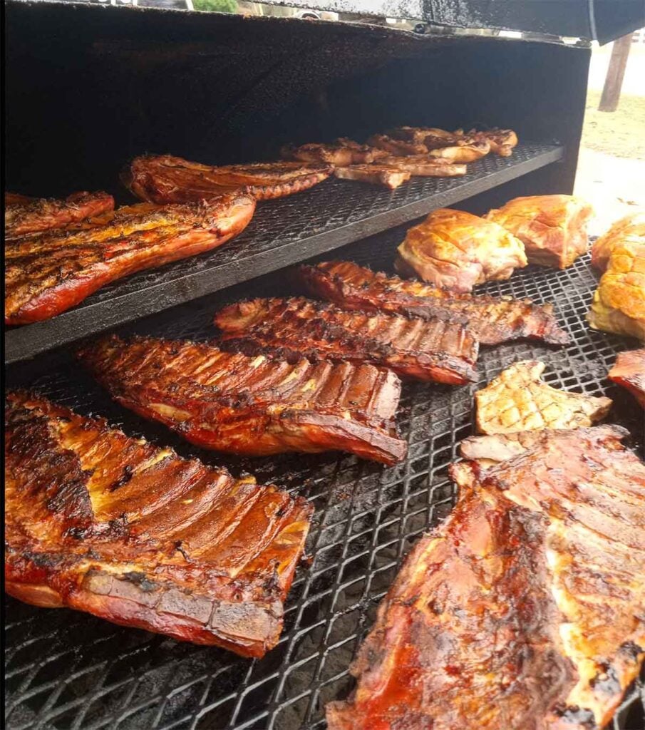 Racks of pork ribs smoking over charcoal and wood embers.