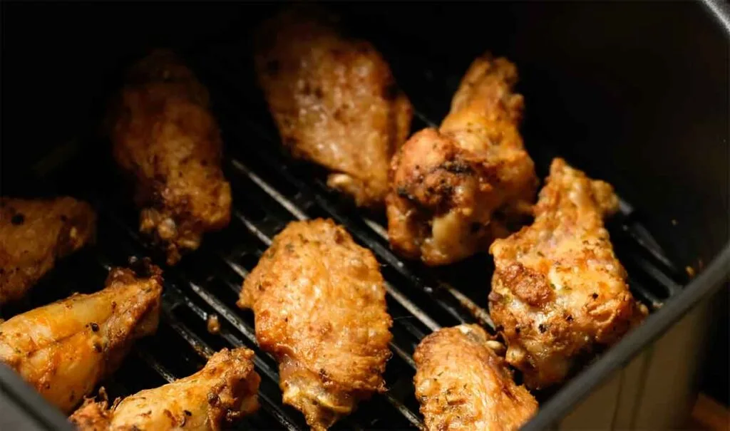 Wings in an air-fryer basket in a single layer with gaps for fast reheating and a crisp finish.