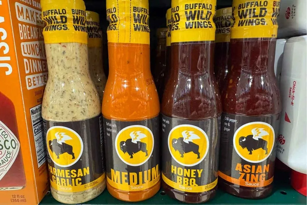 Buffalo Wild Wings bottled sauces on a store shelf, including Parmesan Garlic, Medium, Honey BBQ, and Asian Zing.