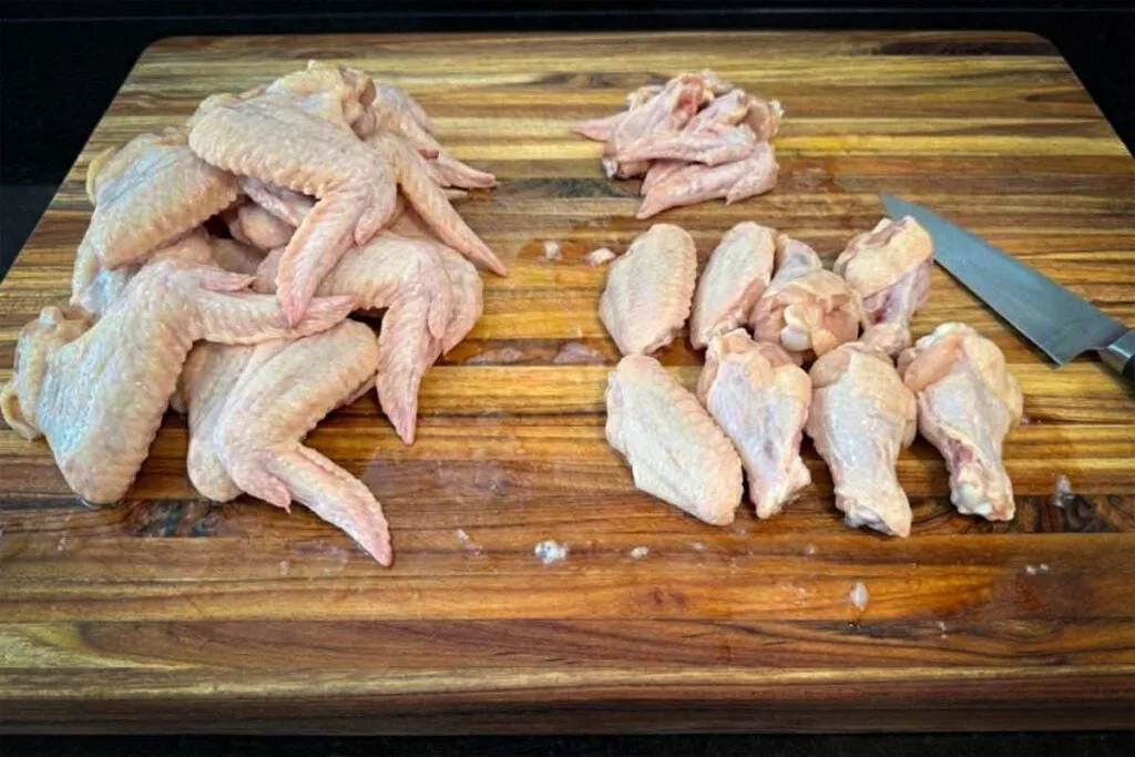 Whole chicken wings with separated flats and drumettes on a cutting board, showing how to turn whole wings into party wings.