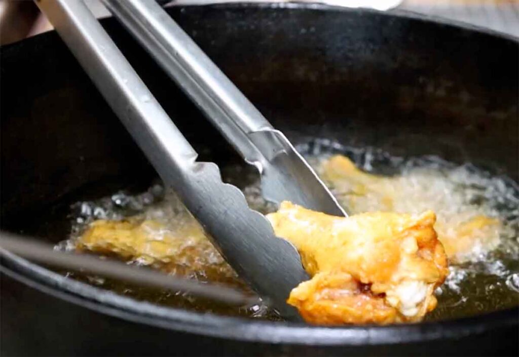 Checking chicken wings in a deep fryer basket during cooking.