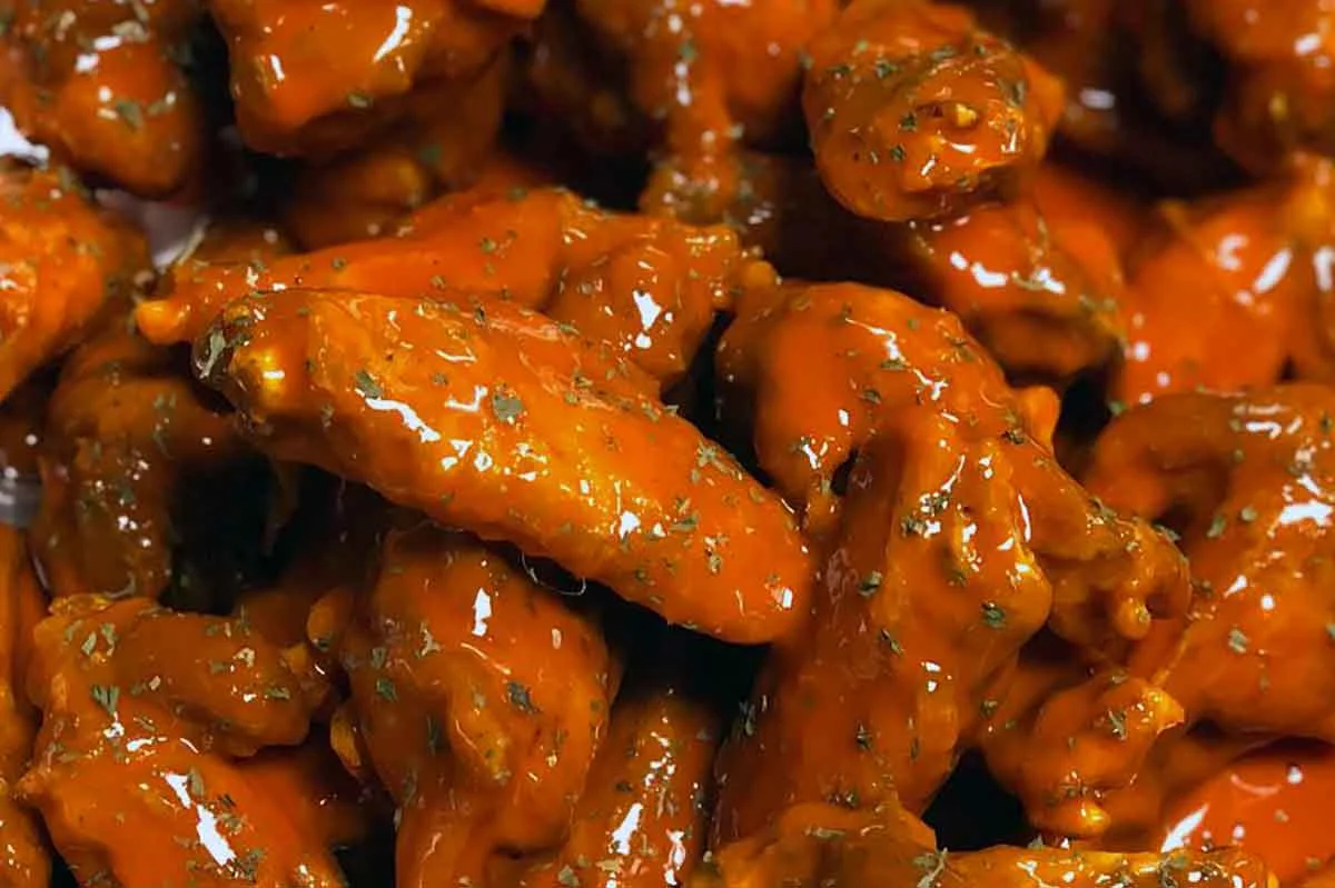Close-up of extra-wet buffalo wings with sauce pooling and dripping.