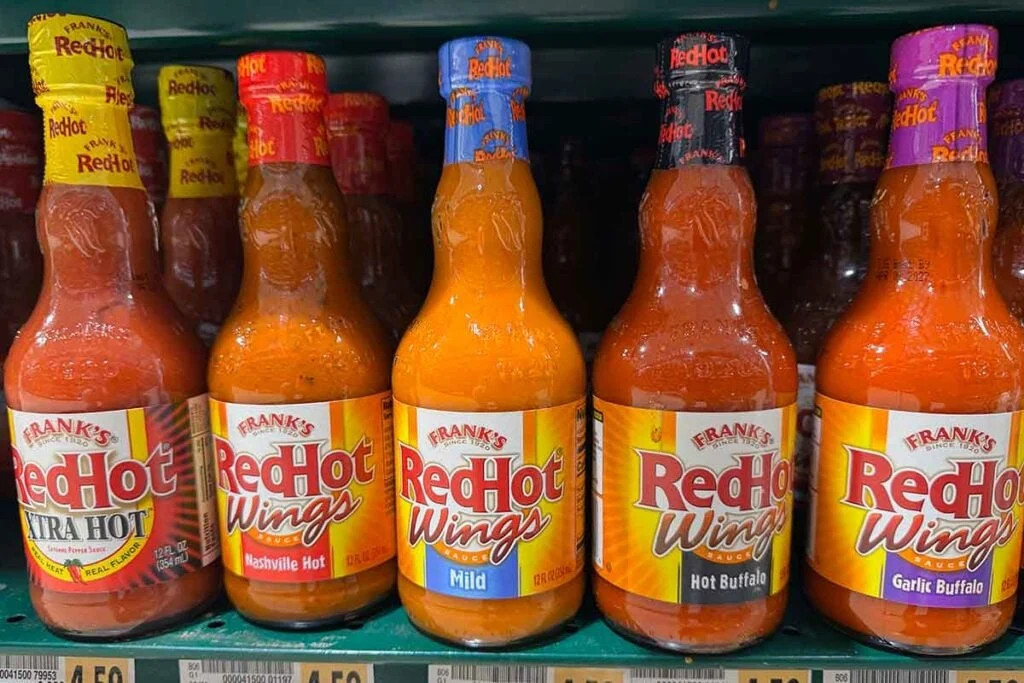Frank&rsquo;s RedHot Wing Sauce bottles on a store shelf, including Xtra Hot, Nashville Hot, Mild, Hot Buffalo, and Garlic Buffalo.