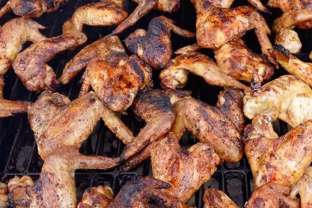 Whole wings reheating on a grill grate, using indirect heat first, then a brief direct-heat crisp finish.