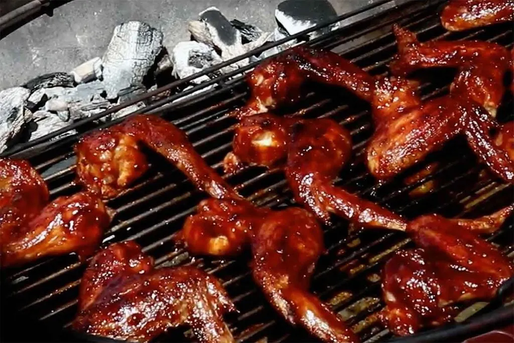 Two-zone charcoal grill with coals on one side and whole wings cooking, showing direct and indirect heat zones.