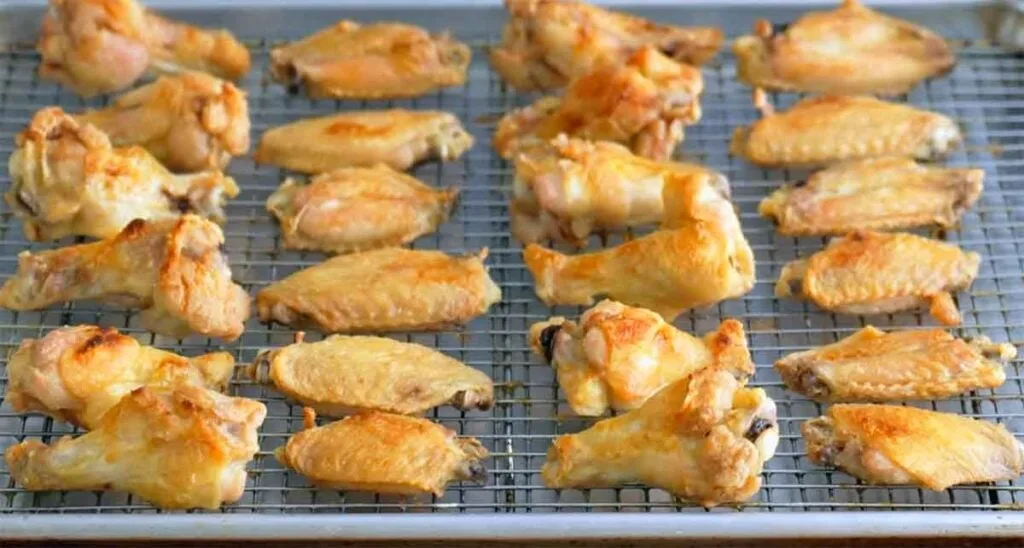 Party-cut wings spaced in a single layer on a rack over a sheet pan for oven reheating and crisp skin.