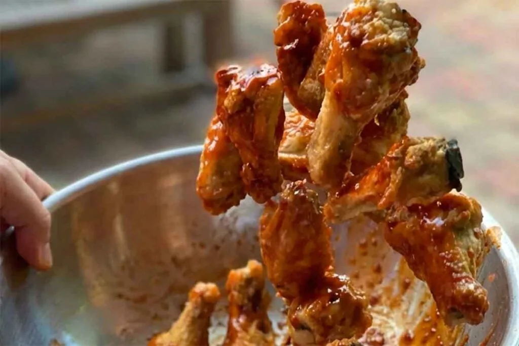 Fried wings mid-toss in a metal bowl with bright buffalo sauce.