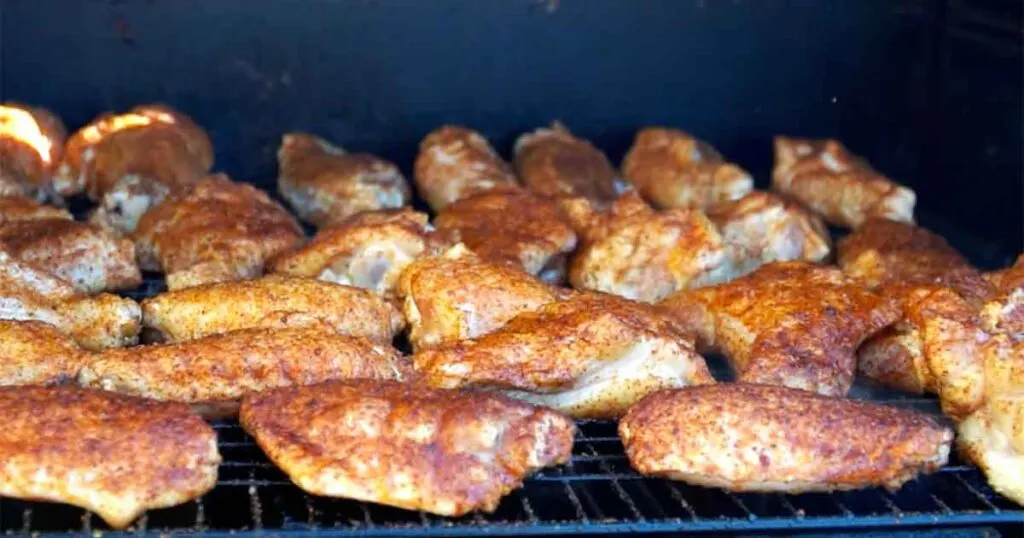Seasoned wings smoking on a rack before a hot finish to bring the skin back crisp.