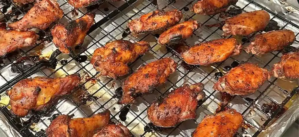 Cooked wings spaced on a wire rack over a sheet pan so air flows and steam escapes during holding.