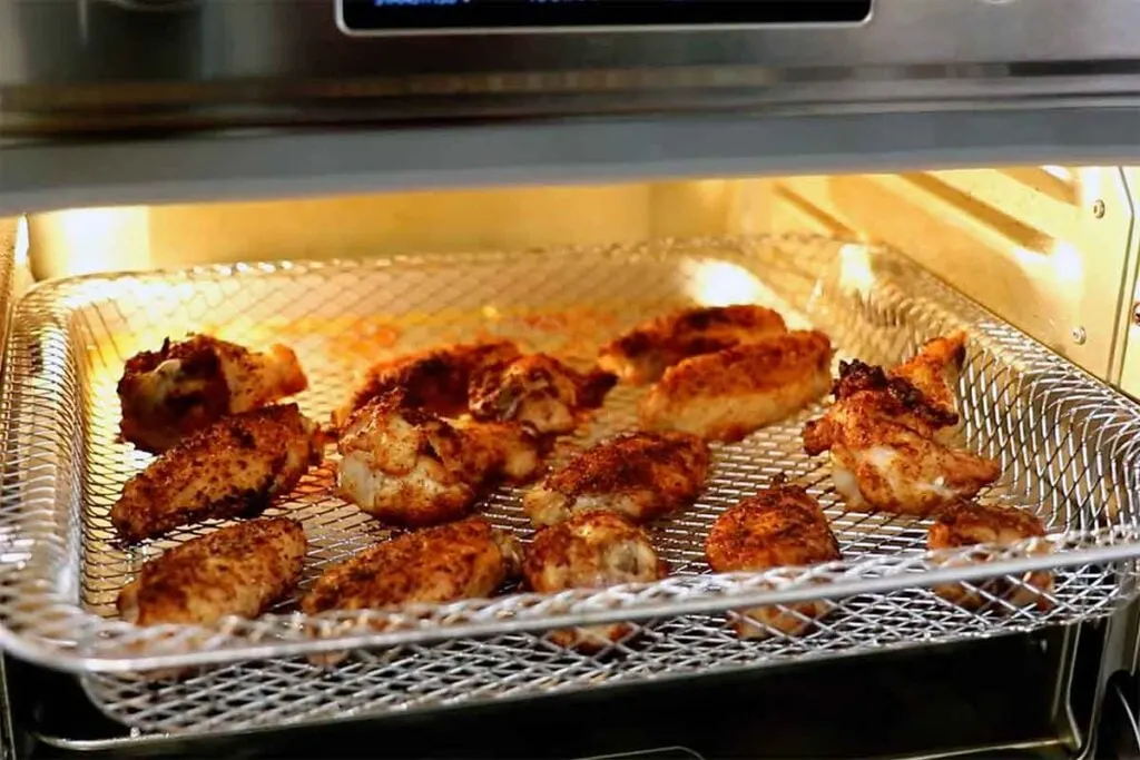 Wings reheating on a mesh tray in a toaster oven so hot air can circulate and re-crisp the skin.