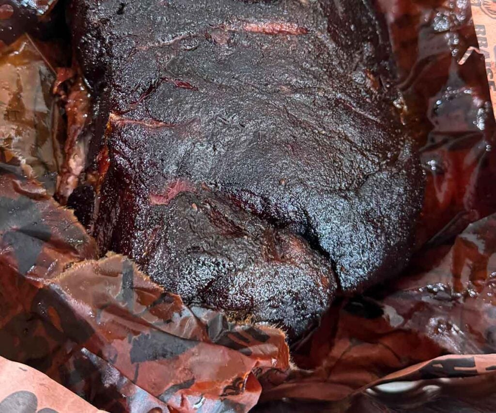 Smoked pork butt resting in butcher paper with dark bark visible after the wrapping stage of the cook.