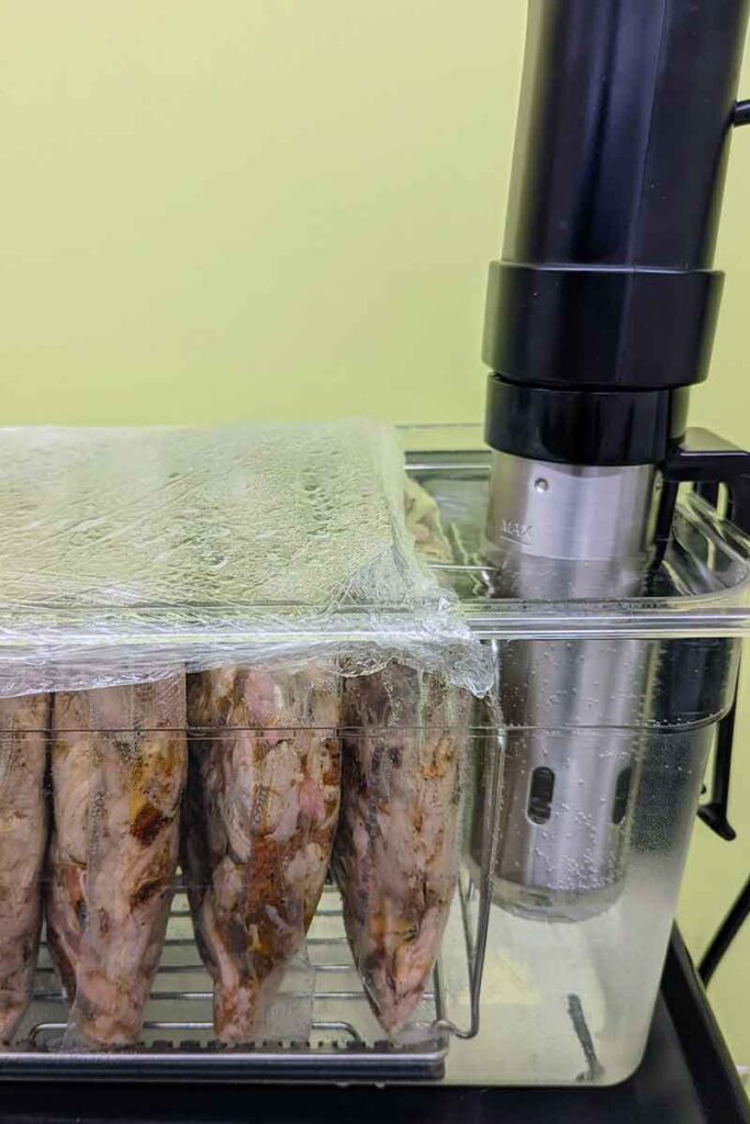 Vacuum-sealed pulled pork reheating in a sous vide water bath with an immersion circulator.