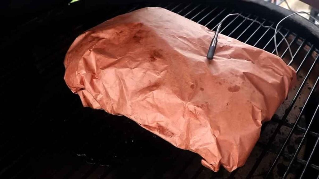 Pork butt wrapped in butcher paper on a smoker, showing the middle-ground method for bark and timing.