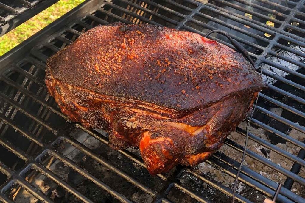 Unwrapped pork butt smoking with bark forming, showing the bark-first tradeoff of a no-wrap cook.
