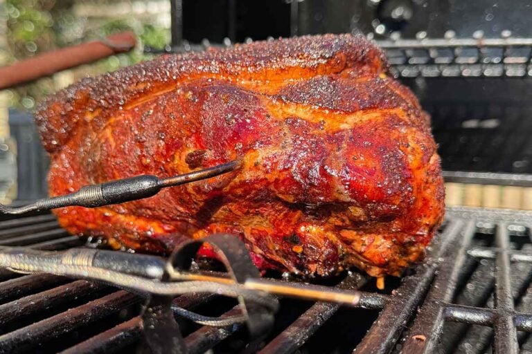 Pork butt on a smoker with a leave-in probe inserted as bark sets during a low-and-slow cook.