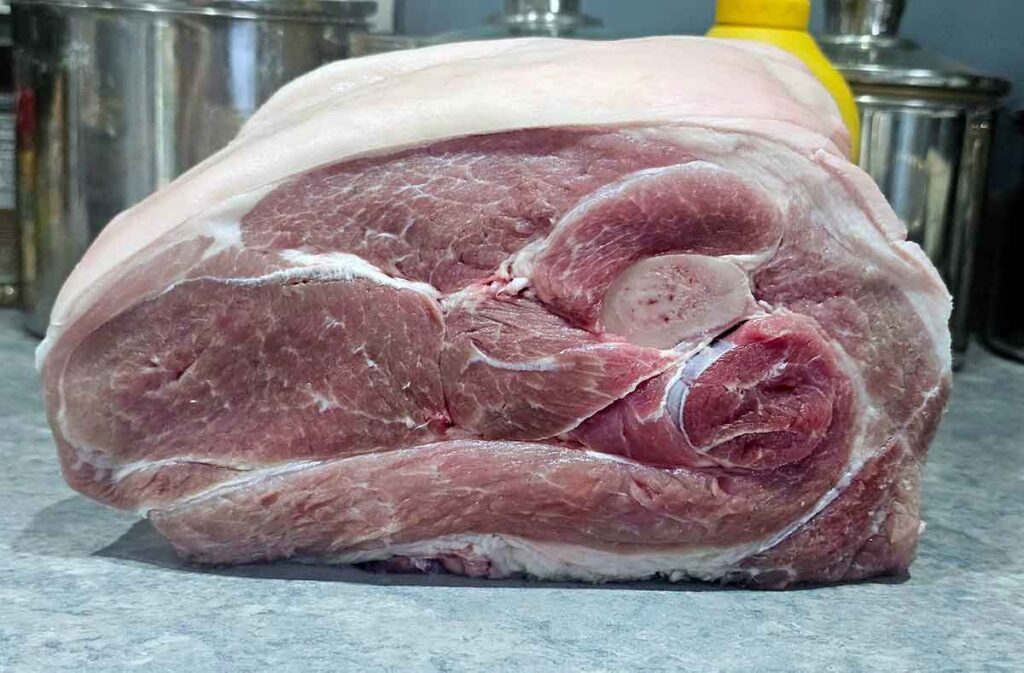 Raw skin-on picnic shoulder with bone visible.