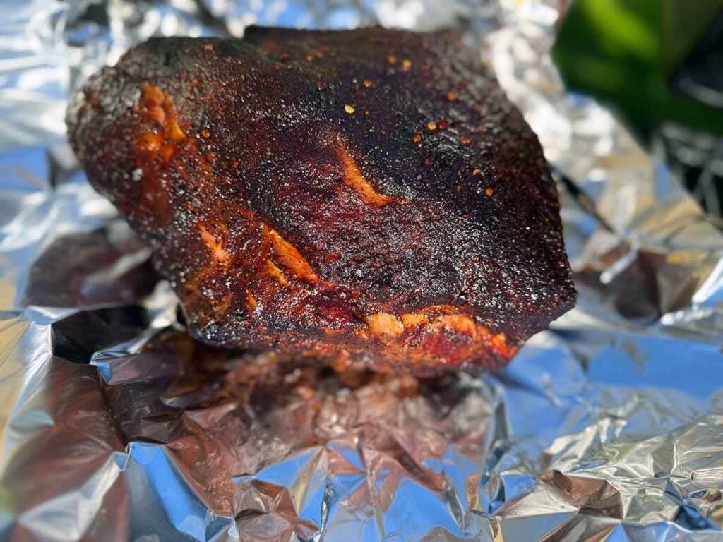 Pork butt with set bark on foil, ready for the wrap decision during a pulled pork cook.