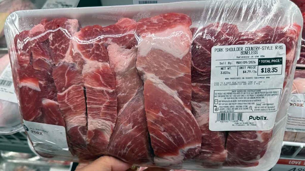 Package of boneless pork shoulder country-style ribs sold near rack ribs in a grocery meat case.