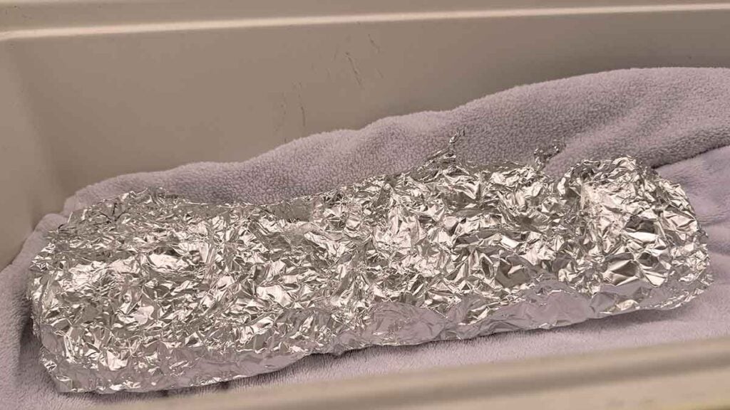 Towel-lined cooler set up to hold foil-wrapped ribs warm before serving.