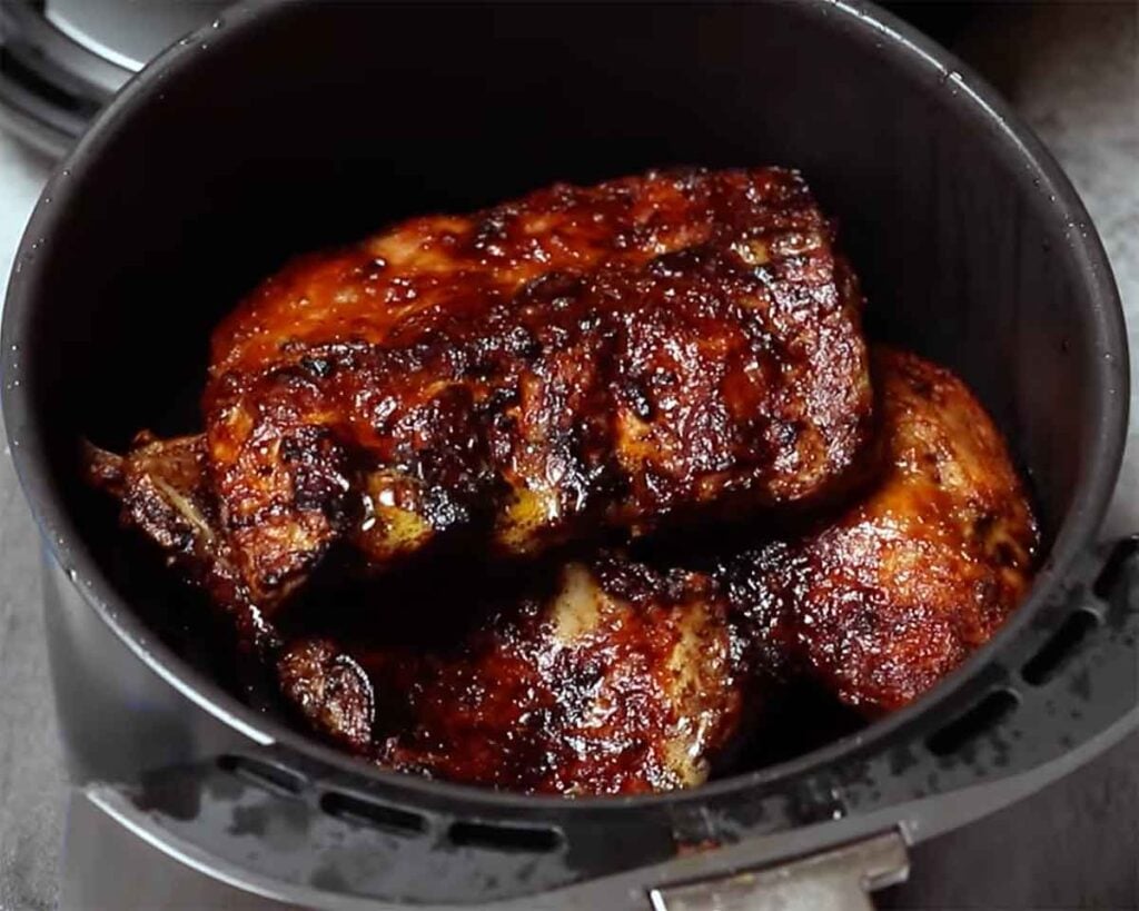 Small portion of sauced ribs reheating in an air fryer basket.