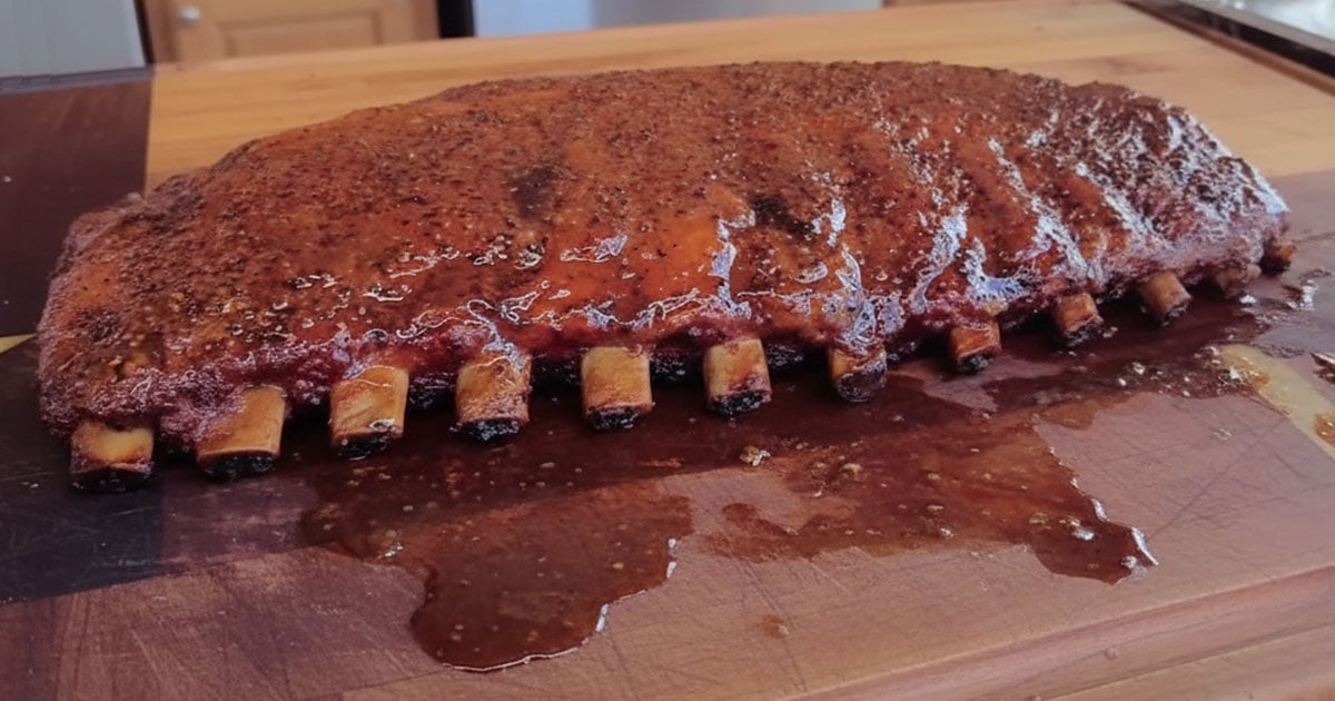 Full rack of cooked pork ribs with visible bone ends along the front edge.