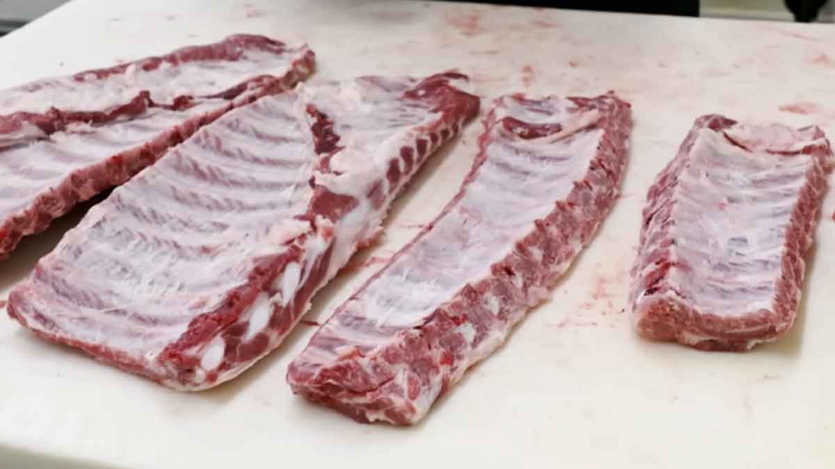 Several raw rib racks on a butcher table, showing how rib size and shape can vary by cut.