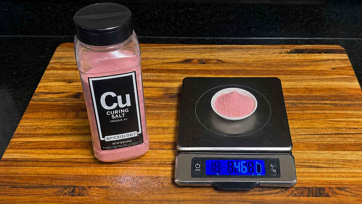 Cure #1 curing salt beside a digital gram scale with pink curing salt measured in a small dish.