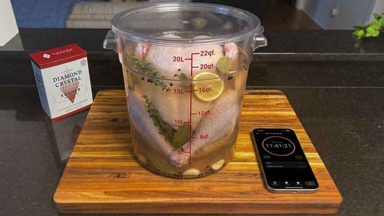 Whole turkey brining in a clear container with kosher salt and a phone timer nearby.