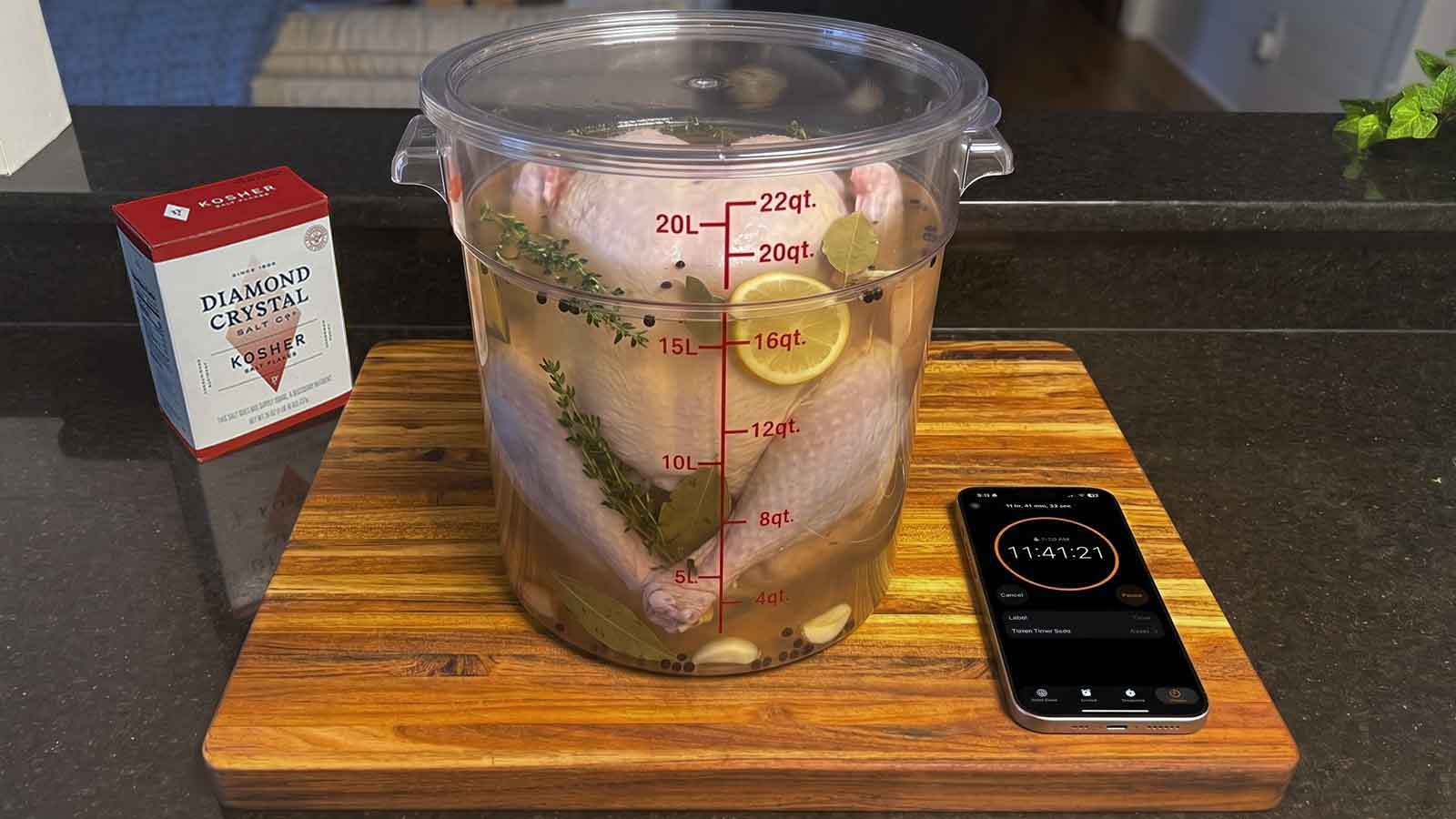 Whole turkey brining in a clear container with kosher salt and a phone timer nearby.