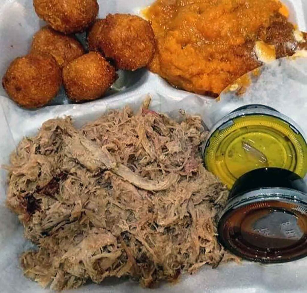 Chopped BBQ plate with sauce cups, sweet potatoes, and hush puppies.
