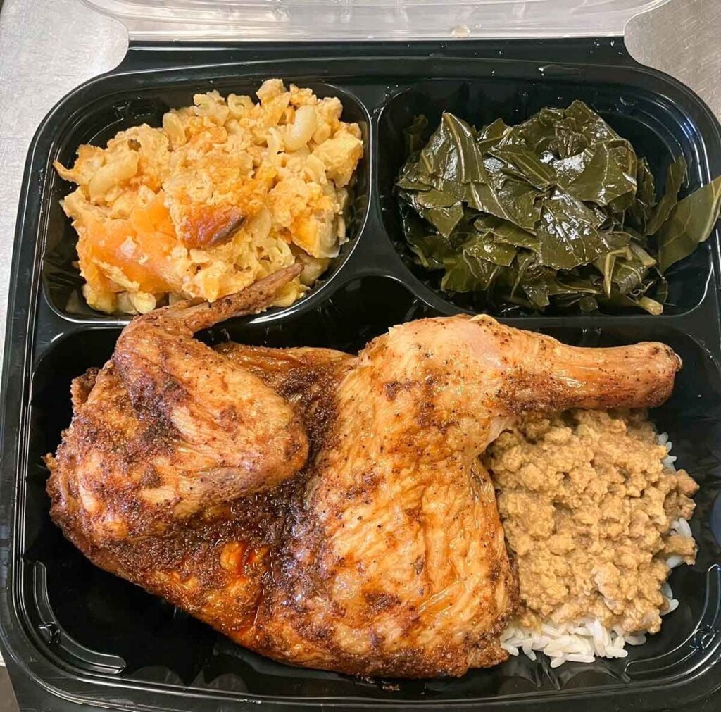 Chicken half with hash, collards, mac and cheese in a to-go container.