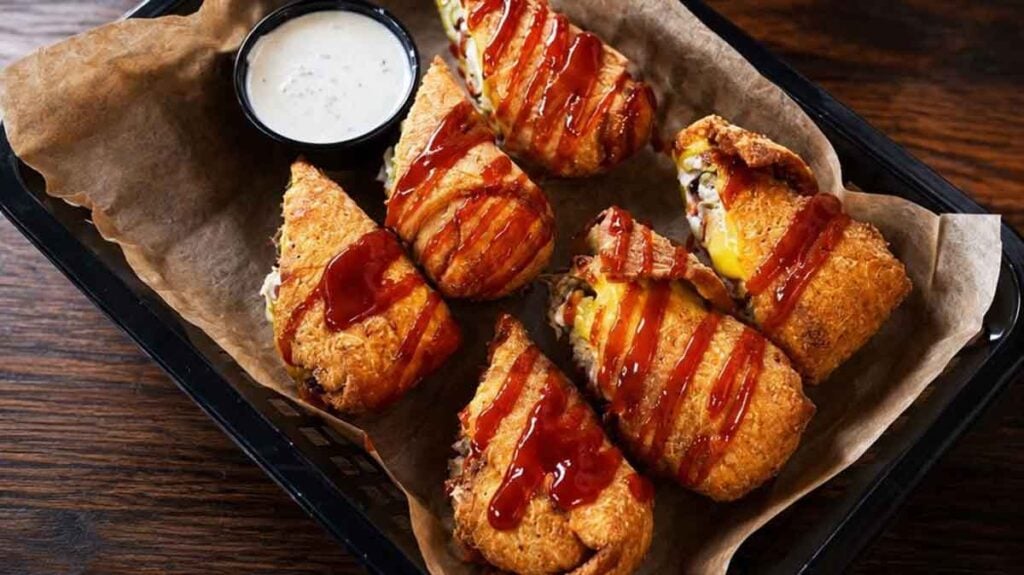 Sliced BBQ eggrolls drizzled with BBQ sauce along side a white dipping sauce.