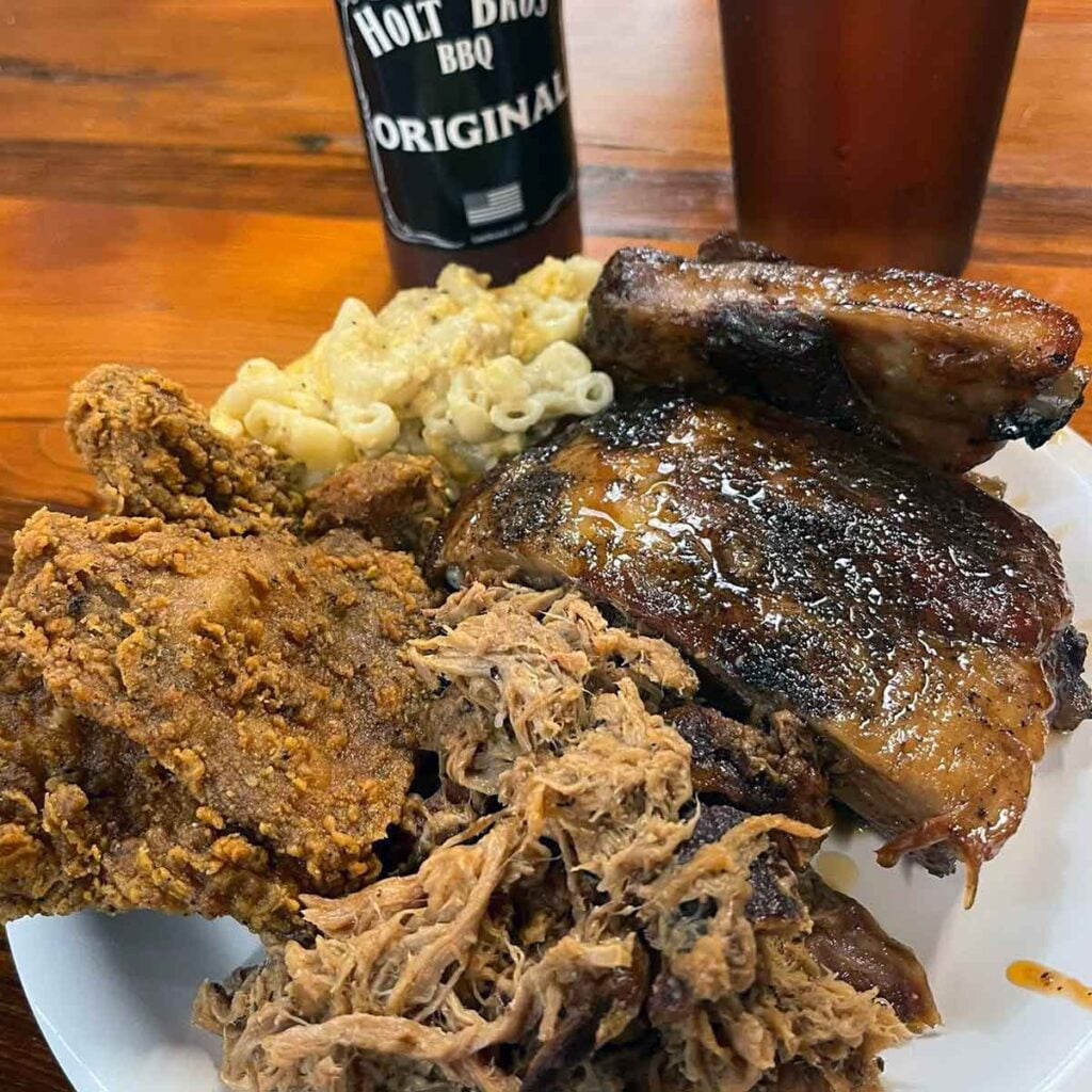 Three meats and Mac and cheese with bottle of BBQ sauce and a drink.