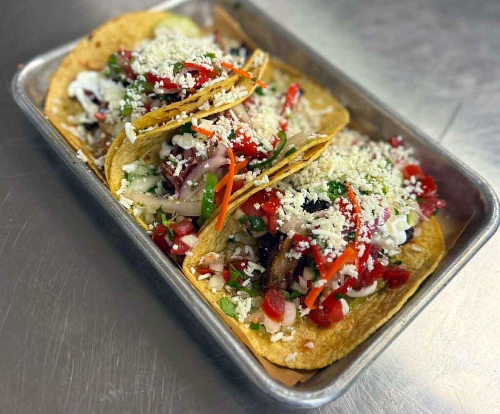 Three tacos on small metal tray.