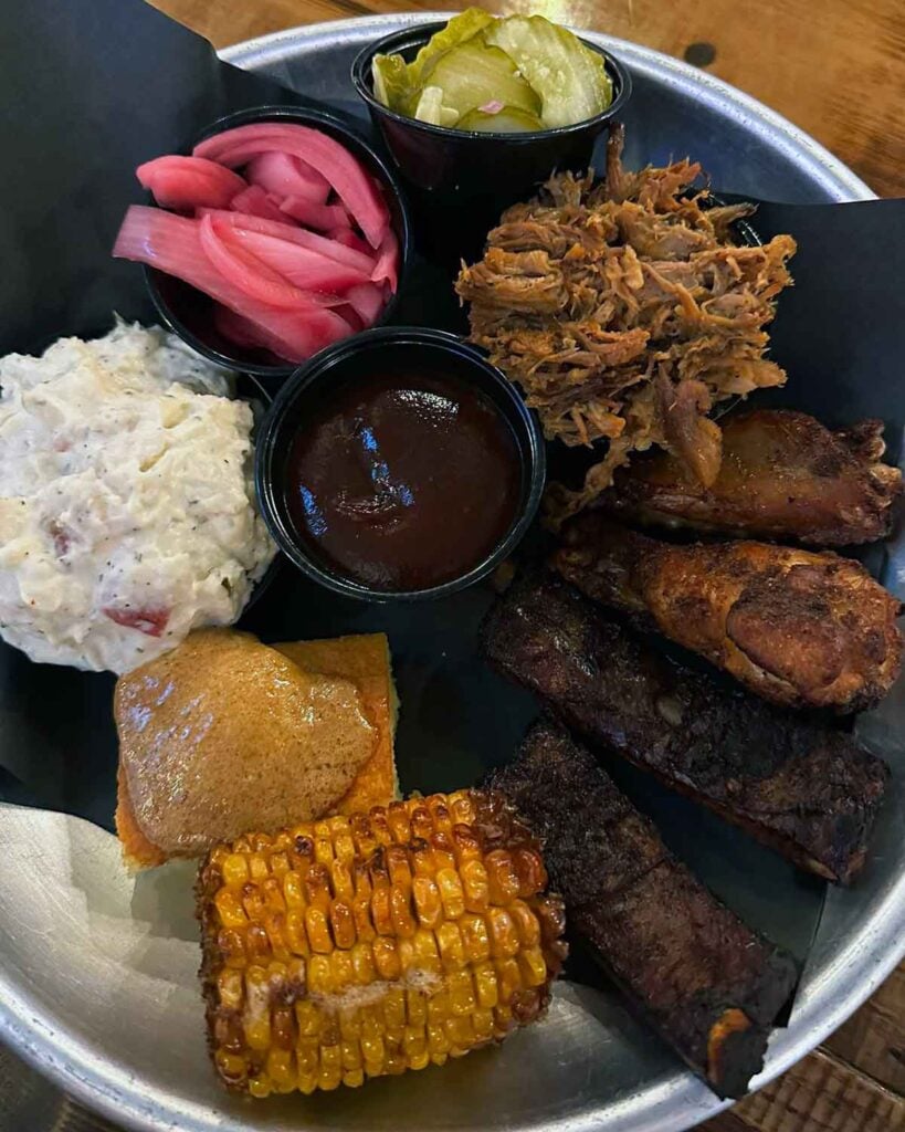 Three meat plate with pulled pork, ribs, and wings with sides.