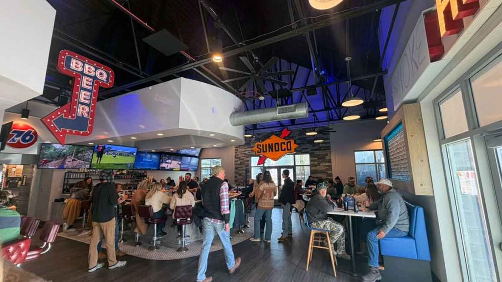 Interior view of Blu Smoke Pit BBQ showing people and BBQ and car-related signage.