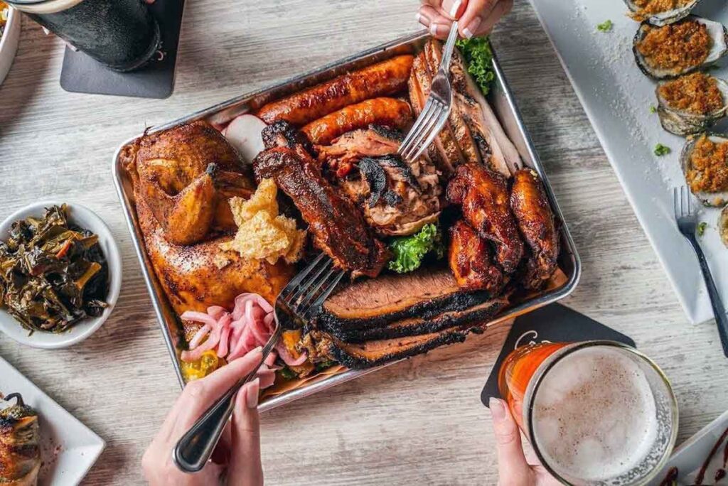 Overhead view of meat sampler platter surrounded by drinks and sides.