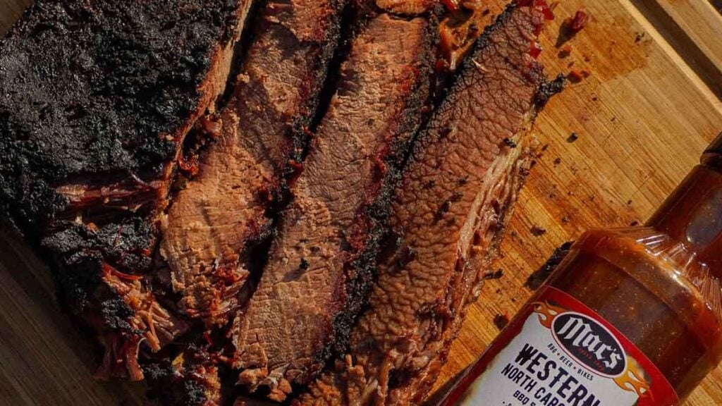 Sliced brisket on cutting board by a bottle of sauce.